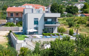 Une maison moderne à deux étages, dotée d’une piscine, d’un patio couvert et offrant une vue sur la verdure environnante.