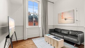 A modern living room with a grey leather sofa, a white coffee table, and a painting on the wall. - Luxury 1BD Rittenhouse Sq. | Hosted By Stay Rafa (Philadelphia)