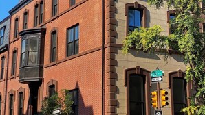 Un immeuble en briques de plusieurs étages, avec une entrée d’angle bien visible, une enseigne indiquant la 20e rue, et un panneau signalant une piste cyclable.