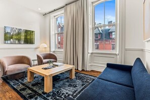 Un salon moderne avec une table basse en bois, deux fauteuils, un canapé et de grandes fenêtres avec des rideaux.