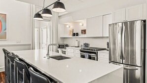 Une cuisine moderne dotée d’un îlot central, d’appareils électroménagers en acier inoxydable et de luminaires suspendus.