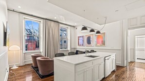 Une cuisine moderne dotée d’un grand îlot central, de meubles blancs et offrant une vue sur la ville grâce à de grandes fenêtres.