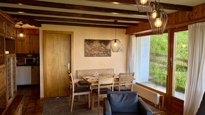 A dining area with wooden furniture, a painting on the wall, and a view of greenery outside.