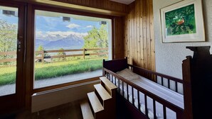 A room with a wooden bench, a view of mountains, and a framed picture on the wall.