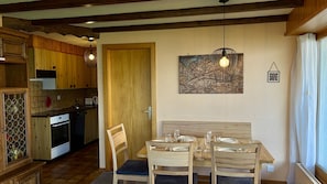 A dining area with wooden furniture, a painting, and a kitchen in the background.