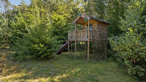 A wooden playhouse with a slide, surrounded by dense greenery. - Awesome home in Højby with WiFi (Højby)