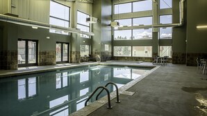 Une grande piscine intérieure aux parois en verre transparent, dotée de nombreuses fenêtres et d’un sol carrelé.