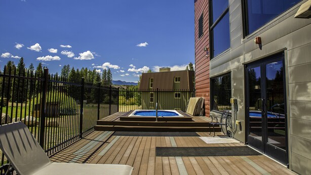 Une terrasse en bois avec un jacuzzi, un banc et une clôture en métal.