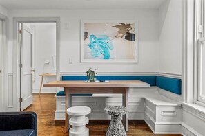 A modern dining area with a wooden table, blue cushioned bench, and a unique abstract painting on the wall.