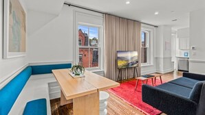 A modern living room with a wooden table, blue and white seating, a red rug, and a large window with curtains. - Luxury in Ritt Sq. | Parking | Hosted By StayRafa (Philadelphia)
