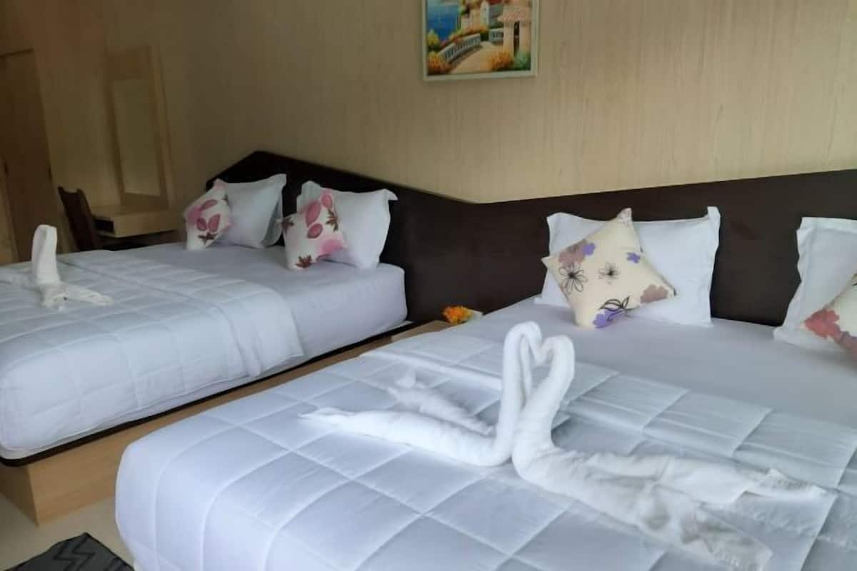 Two beds with white linens and swan-shaped towels, a dark headboard, and a painting on the wall.