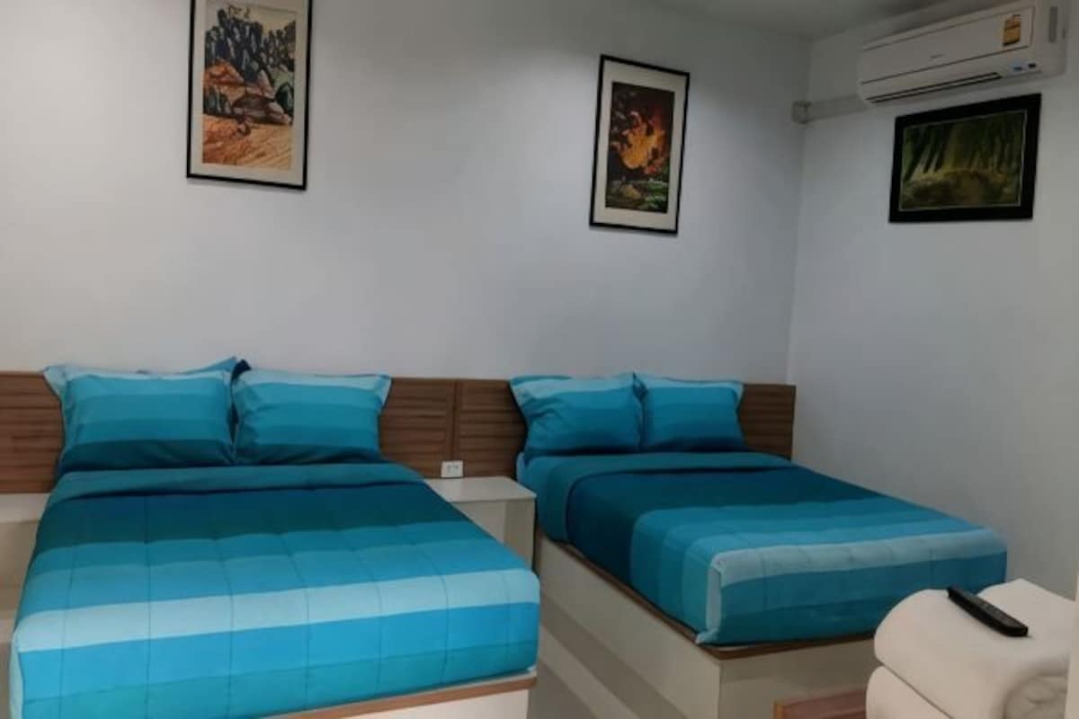 A room with two beds, each with blue bedding, a white chair, and framed pictures on the walls.