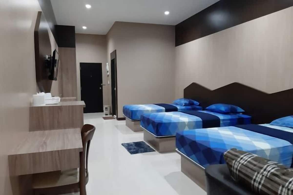 A modern hotel room with three beds, a desk, and a chair.
