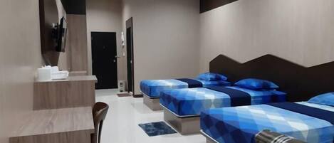 A modern hotel room with three beds, a desk, and a chair.