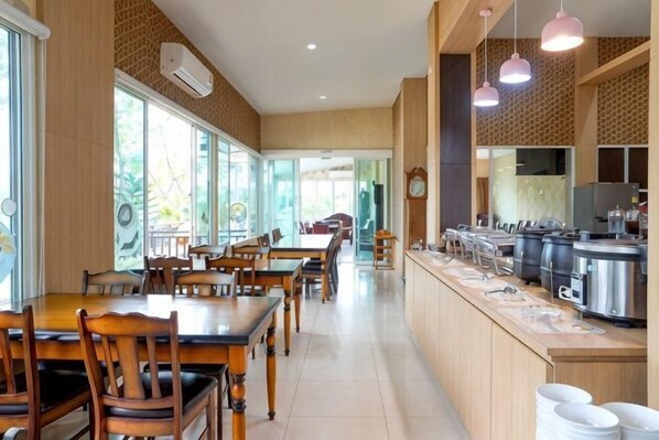 A spacious dining area with wooden tables and chairs, a long counter with kitchen appliances, and large windows providing natural light. - Tho Mai Resort (Khlong Yai)