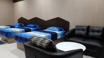 Habitació d'hotel moderna amb dos llits, un sofà de pell negra i una taula petita blanca.