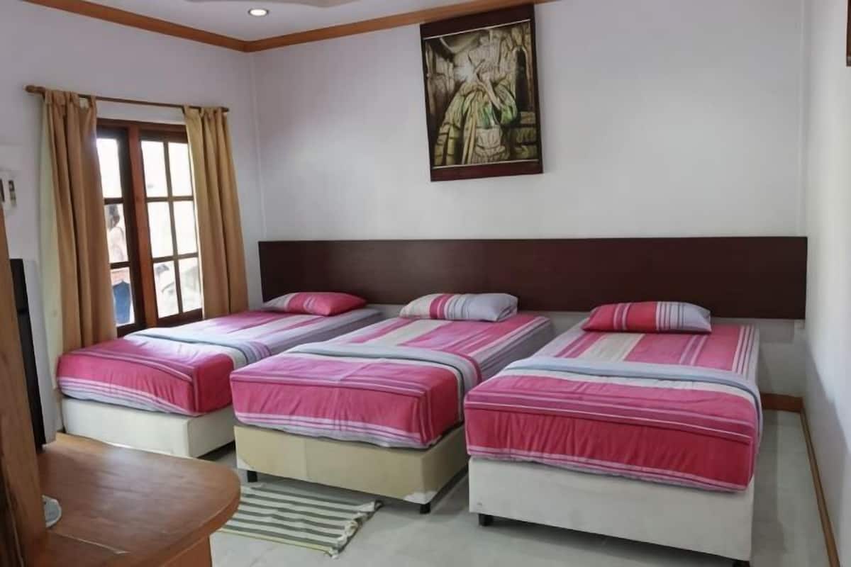A hotel room with three beds, a wooden headboard, a painting on the wall, and a window with curtains.