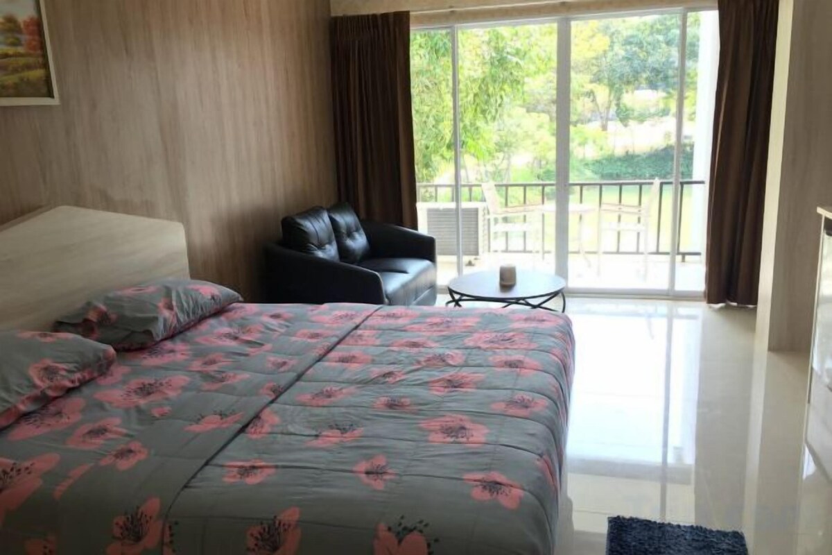 A hotel room with a bed, a chair, a small table, and a balcony with a view.