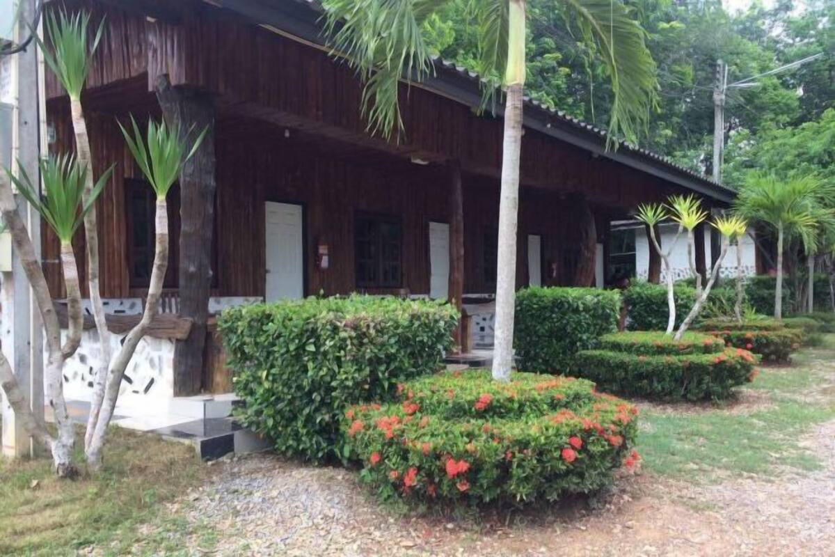 A wooden building with a covered porch, surrounded by well-maintained hedges and flowering plants.