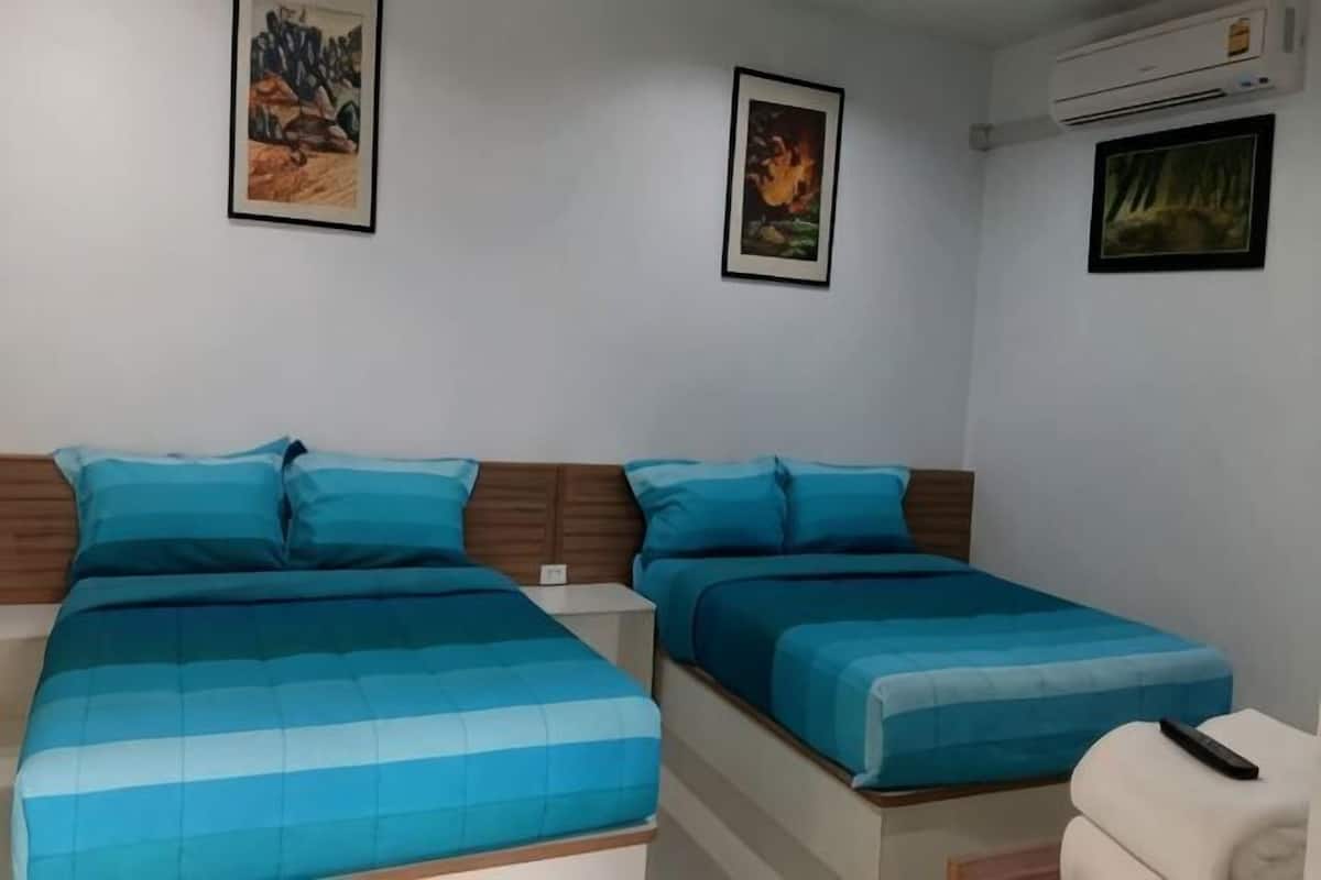 A room with two beds, each with blue bedding, a white chair, and framed pictures on the walls.
