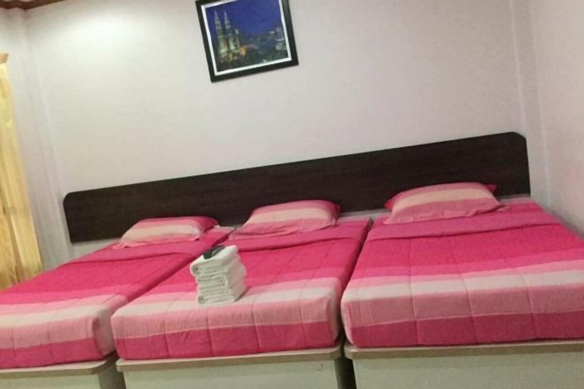 A room with three beds, each with pink bedding and white pillows. There is a framed picture on the wall above the beds.