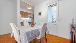 A dining area with a table set for two, a kitchen in the background, and a view through a door. - 1 bedroom gorgeous apartment in Zadar (Zadar)