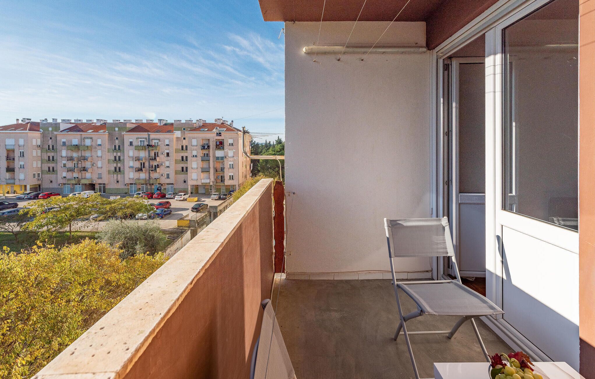A balcony with a chair and a table, overlooking a parking area and residential buildings.