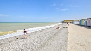 Una playa de guijarros con una hilera de coloridas cabañas de playa a la derecha.