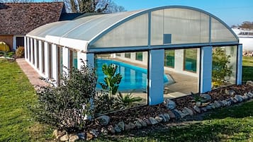 Une serre dotée d’un toit transparent, d’une piscine et d’un espace jardin aménagé avec des rochers et des plantes.