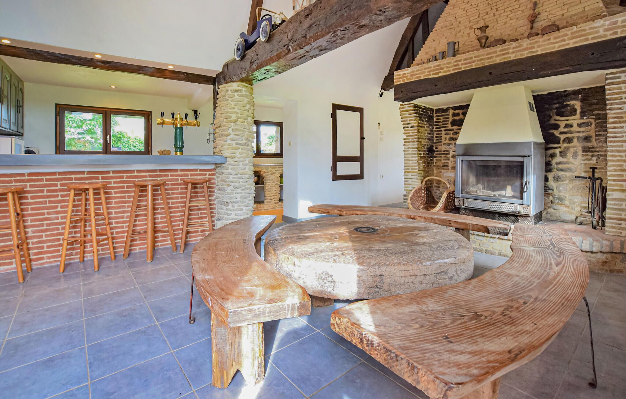 Une cuisine rustique avec une cheminée en pierre, des tabourets en bois et une grande table en bois.