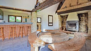 A rustic kitchen with a stone fireplace, wooden stools, and a large wooden table. - Stunning home in Grandmesnil (Grandmesnil)