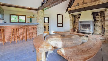 Une cuisine rustique avec une cheminée en pierre, des tabourets en bois et une grande table en bois.