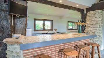 Une cuisine dotée d’un plan de travail en pierre, de tabourets en bois, d’un mur en briques et d’une fenêtre donnant sur un paysage verdoyant.