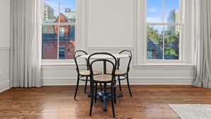 Une pièce comprenant une table à manger et des chaises, de grandes fenêtres avec des rideaux et un plancher en bois.