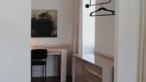Un couloir avec un mur blanc, un plancher en bois foncé, un bureau avec une chaise et un luminaire suspendu.