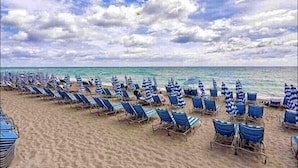 Une plage bordée de rangées de chaises longues bleues et de parasols à rayures, donnant sur l’océan.