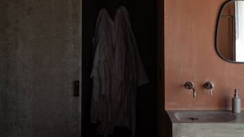 Un baño con pared de concreto, tocador de madera, espejo y lámpara colgante.