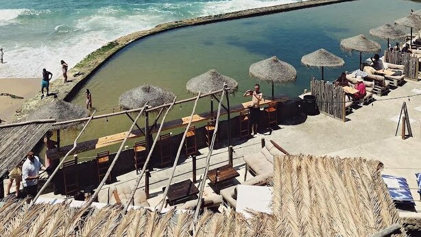 Uma praia com piscina, guarda-sóis e espreguiçadeiras.
