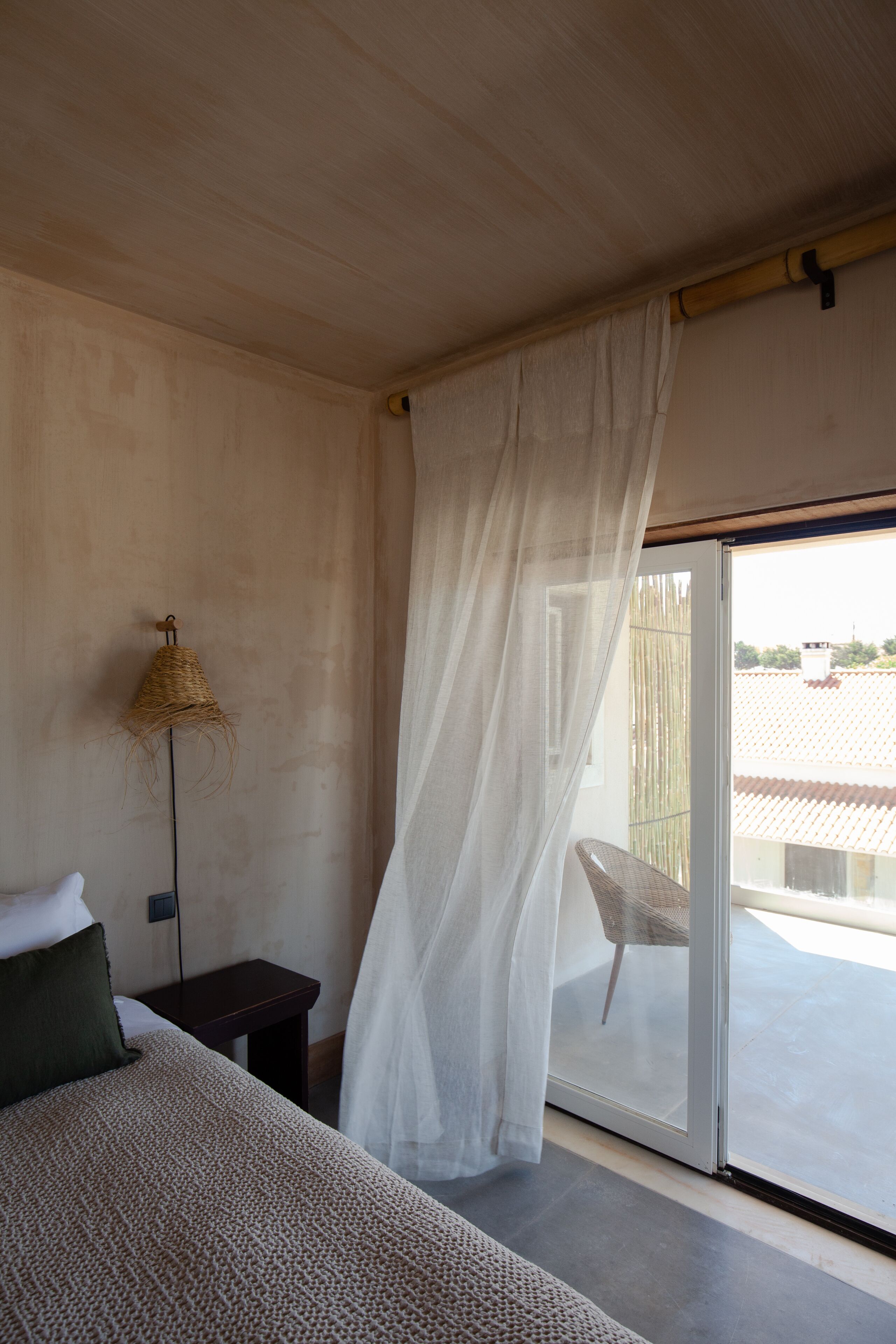 Un dormitorio con cama, mesita de noche, lámpara y puerta corrediza de vidrio que da a un área exterior.