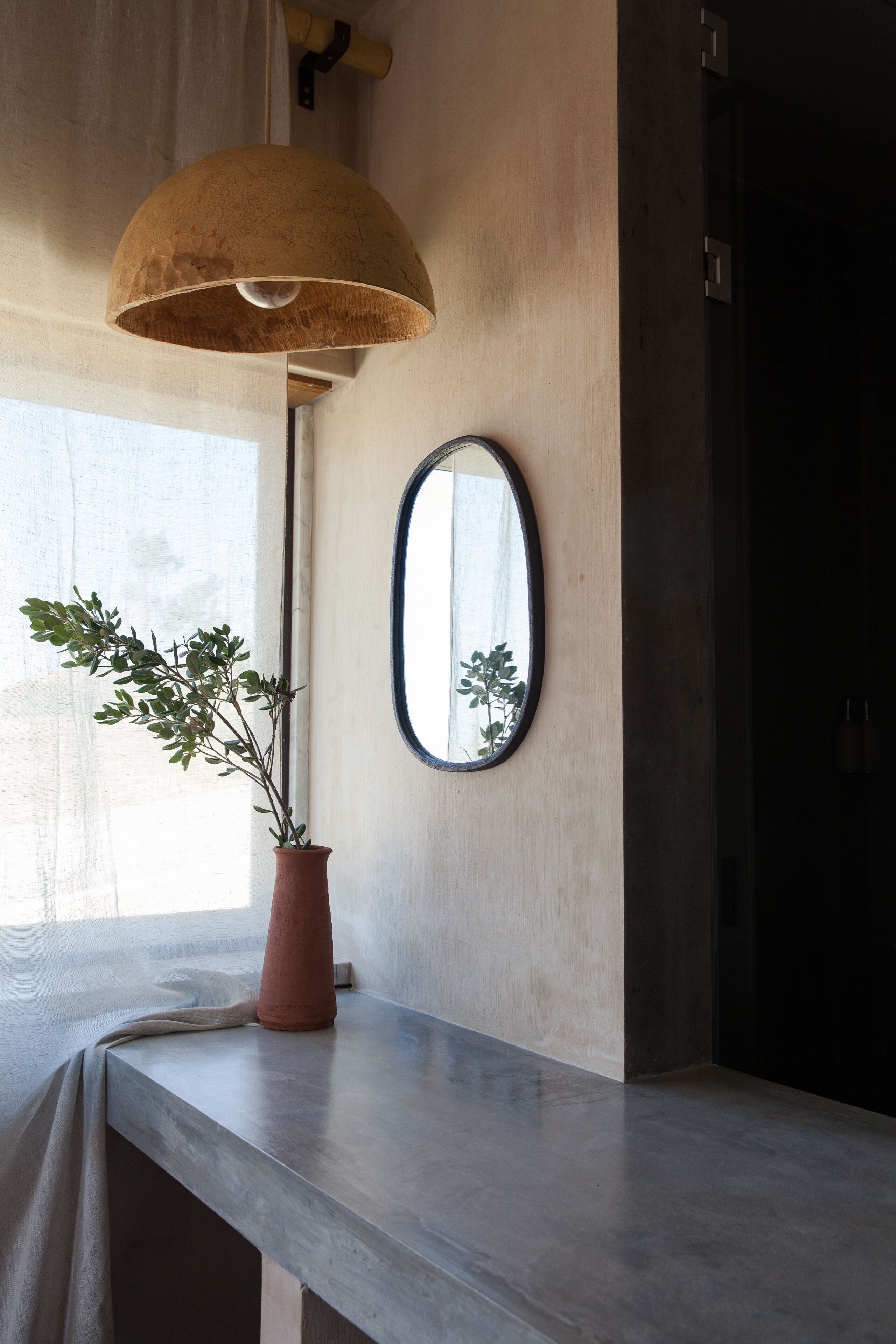 A room with a concrete floor, a potted plant, a large mirror, and a hanging lamp.