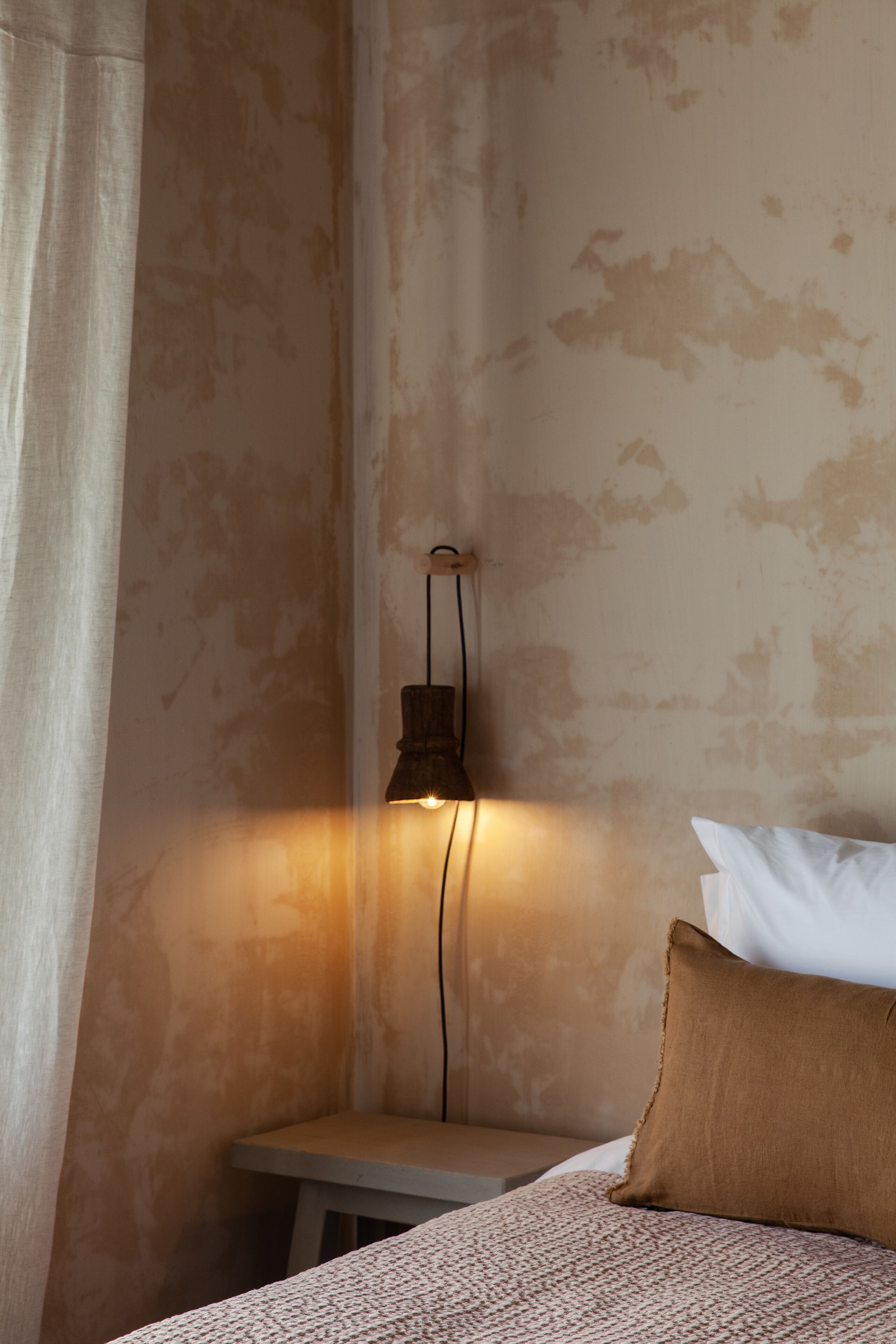 Una habitación con una cama, una mesita de noche y una lámpara de pared.