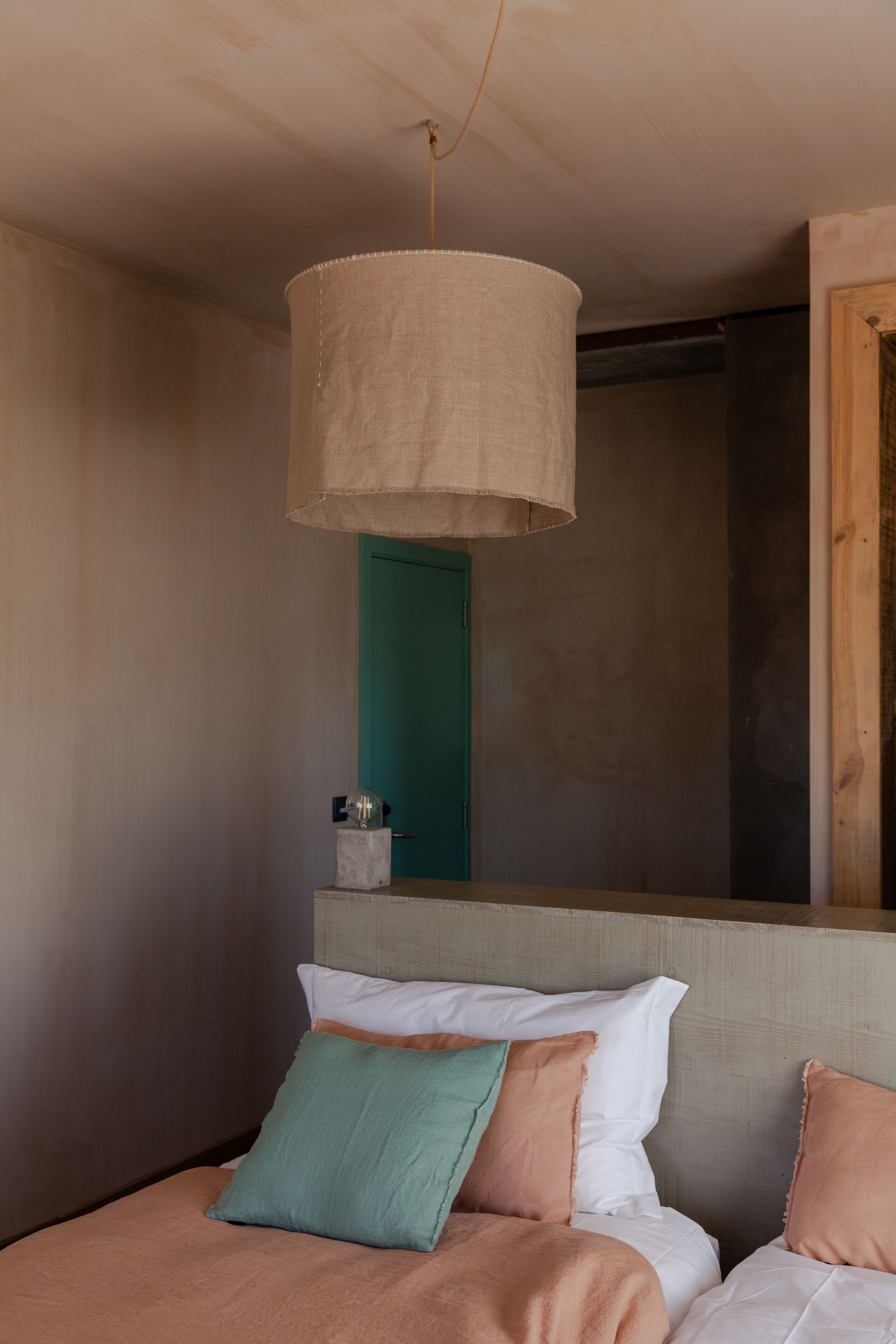A bedroom with a bed, a hanging lamp, a green door, and a wooden wall.