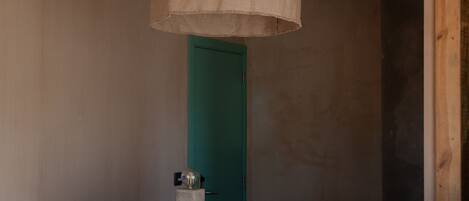 A bedroom with a bed, a hanging lamp, a green door, and a wooden wall.