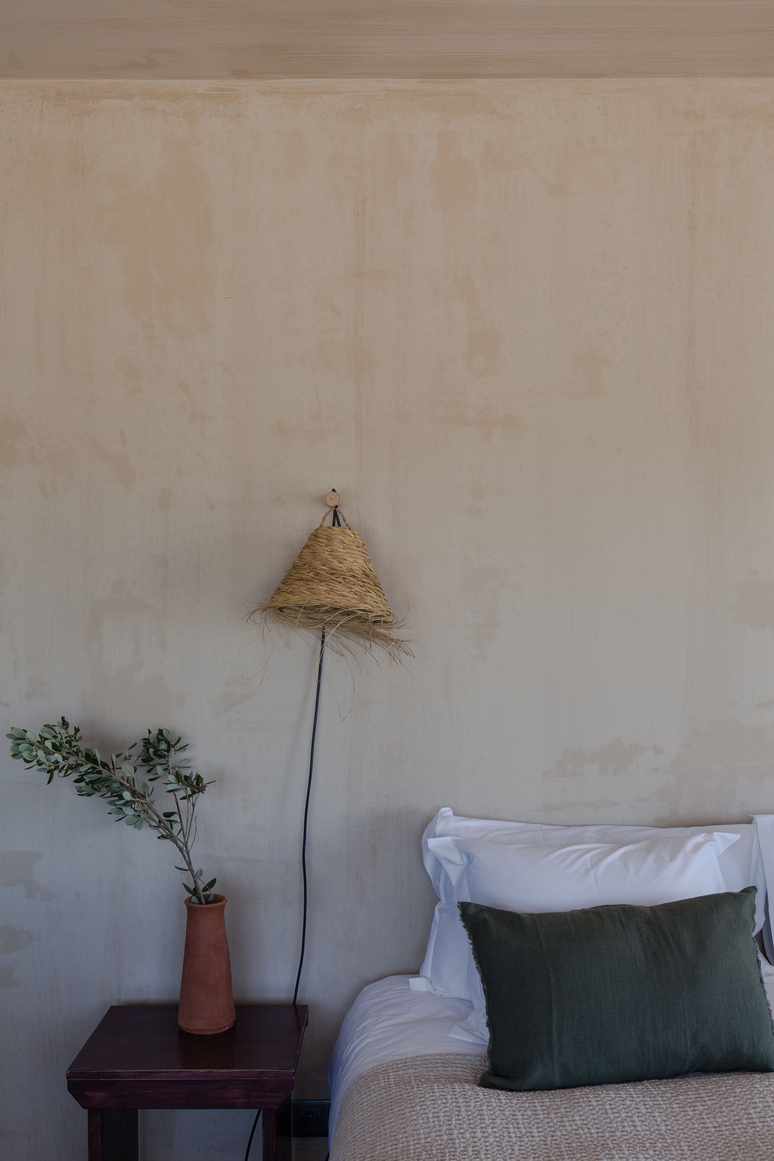 A bedroom with a bed, a bedside table with a potted plant, and a wall-mounted lamp.