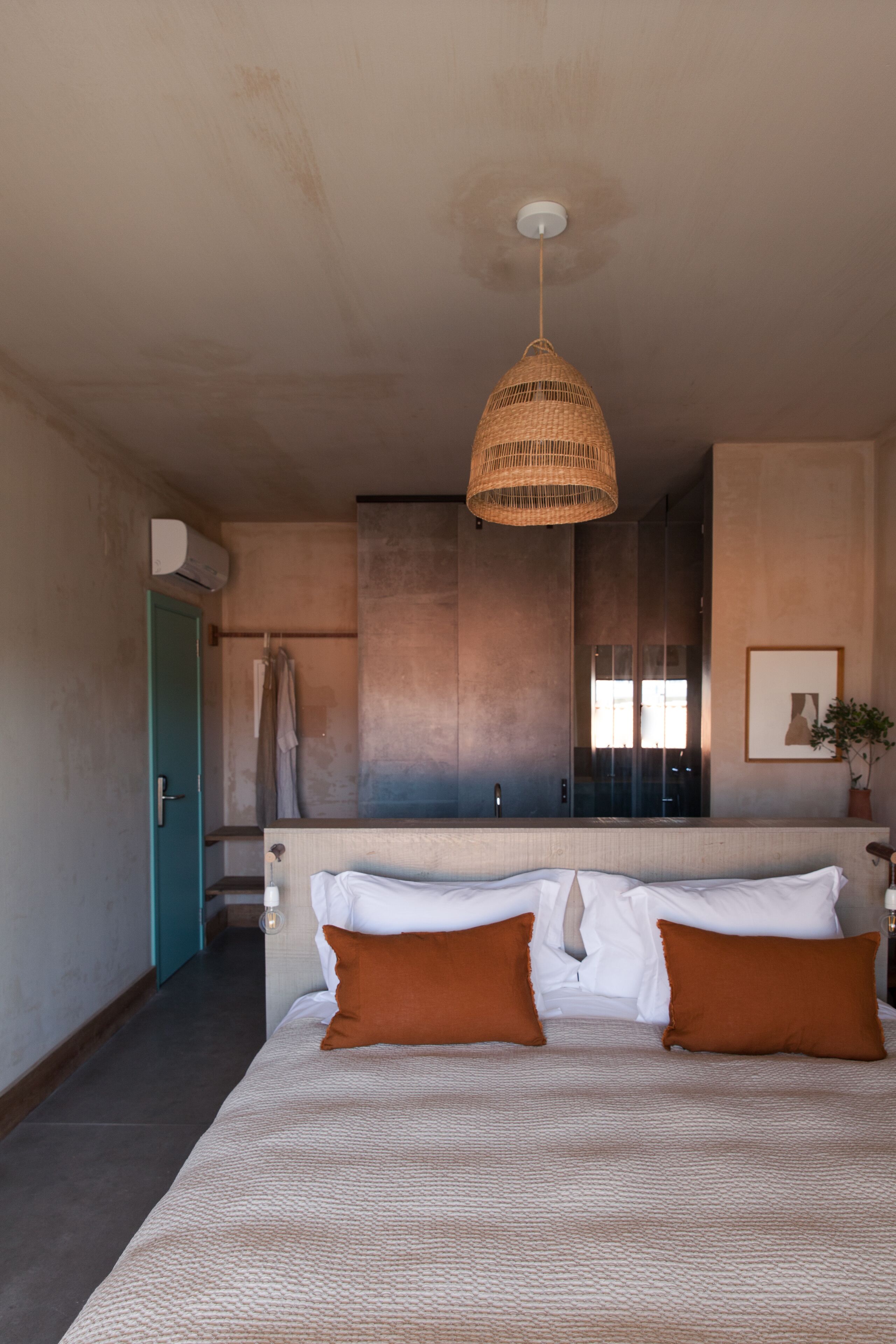 A bedroom with a bed, a hanging light fixture, a bathroom with a mirror, and a door.