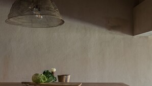 Uma mesa de jantar de madeira com quatro banquetas, um lustre pendurado e uma tigela com legumes.