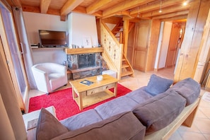 Een knusse woonkamer met een open haard, een bank, een televisie en een trap.