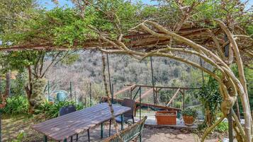 Eine Außenpatio mit Holztisch und -stühlen, umgeben von viel Grün und einer Pergola.