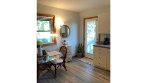 Un coin repas comprenant une table, des chaises, un miroir et une fenêtre avec des stores.
