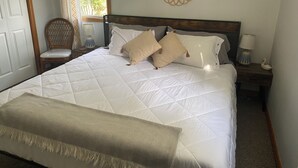 Un lit bien fait, recouvert d’une couette blanche, agrémenté de deux coussins à motifs, d’un miroir décoratif et d’une lampe de chevet.